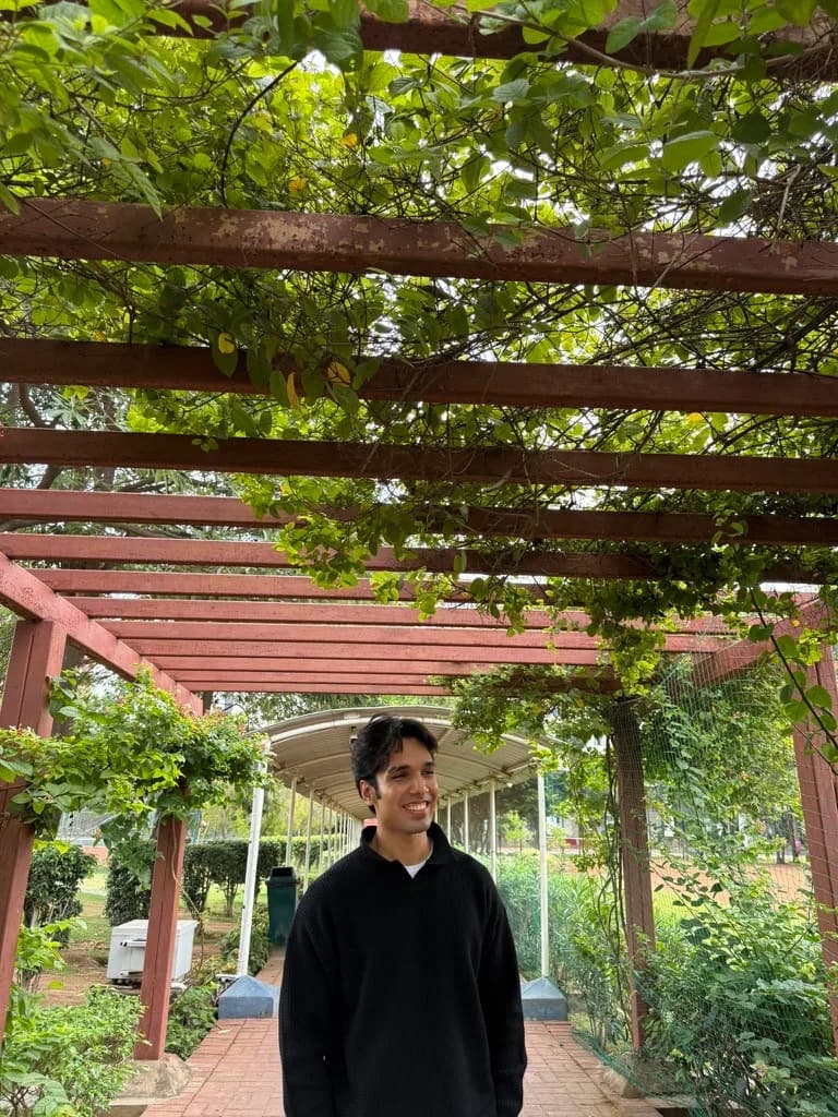 Shivam Tripathi in a waist-up portrait outdoors near a pergola and brick path, smiling slightly off-camera.